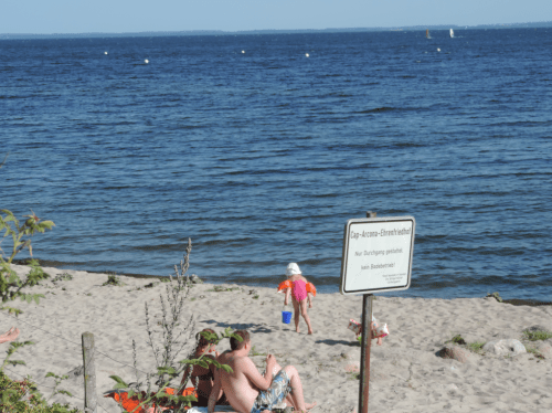 A family on a beach of Neustadt in Holstein July-24, 2013. The view is across the Luebecker Bucht. The posted sign reads "Cap Arcona Ehrenfriedhof. Nur Durchang gestatted. Kein Badebetrieb." It states that this is cemetery, walk-through is allowed, but no other beach activity.