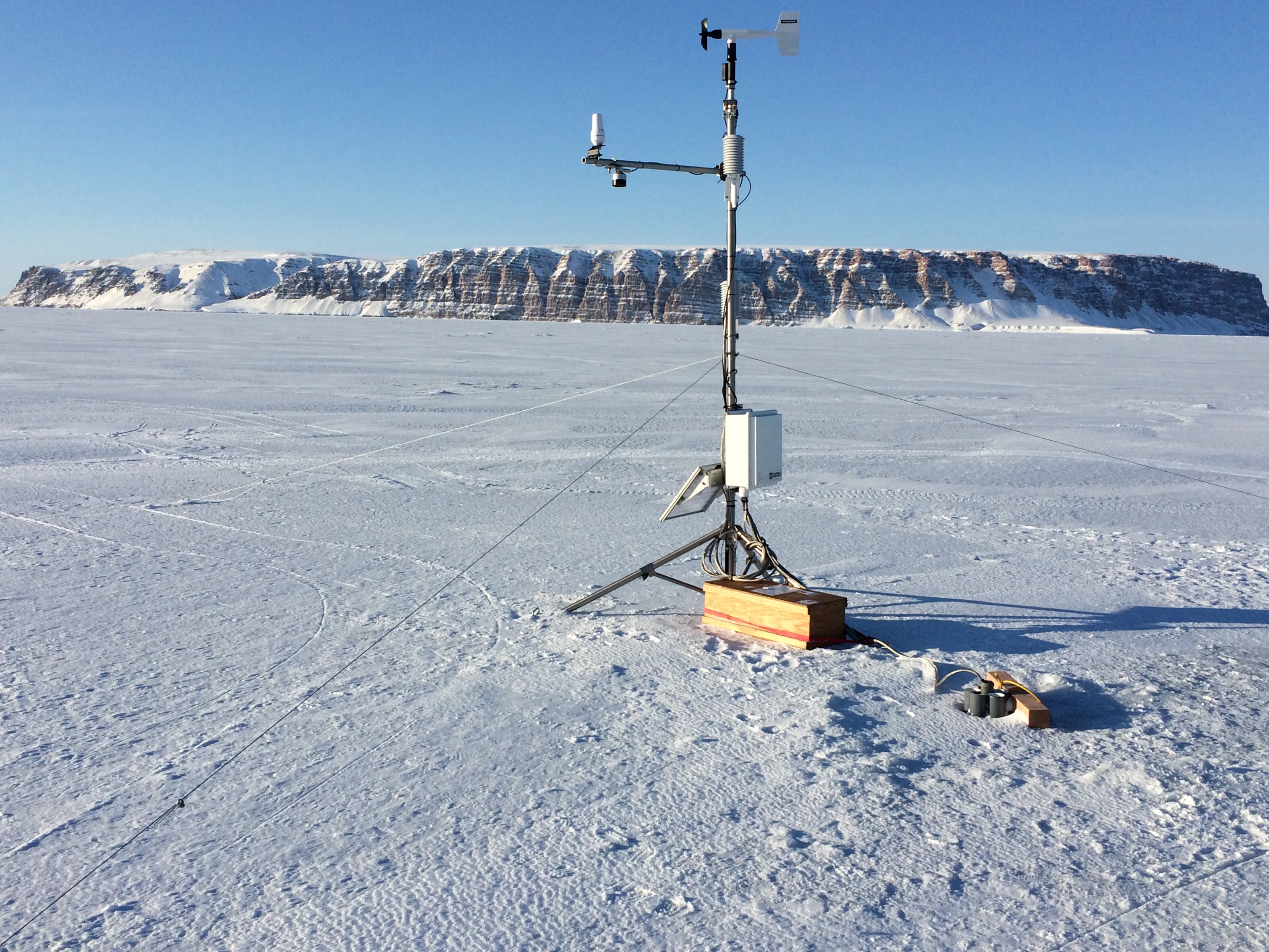 Automated Weather Station on Mar.-23, 2017 near Thule, Greenland. The station includes a satellite antenna to connect to the internet and a cable through the ice to connect to the ocean. Saunders Island is in the background to the west.